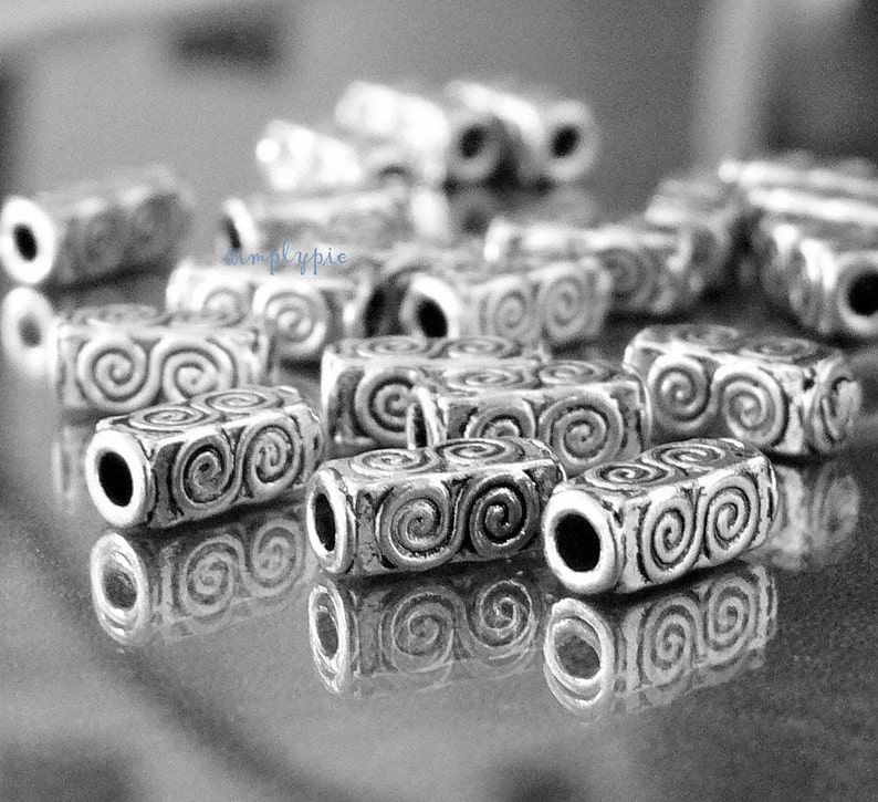 Peut inclure: Gros plan sur des perles en m&eacute;tal argent&eacute; avec un motif en spirale. Les perles sont cylindriques et ont une finition lisse et polie.