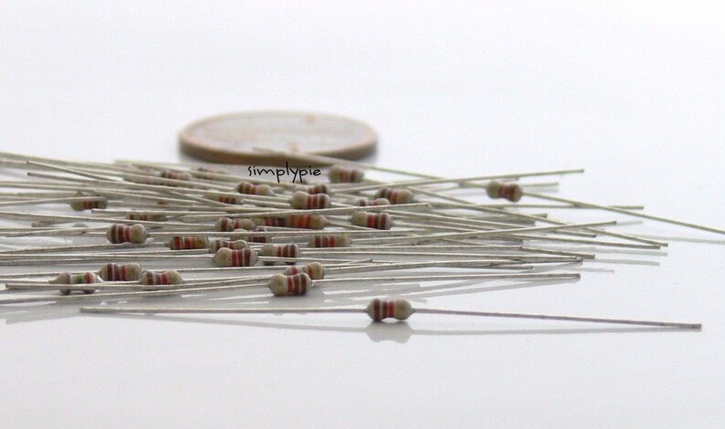 Puede incluir: Una colecci&oacute;n de peque&ntilde;as resistencias electr&oacute;nicas con cuerpos de color canela y bandas de colores, cada una con dos cables met&aacute;licos largos y delgados en los extremos. Una moneda de color cobre se ve al fondo con el texto simplypie.
