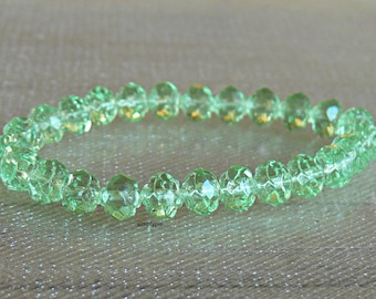 Könnte beinhalten: Ein Armband aus facettierten, hellgrünen Perlen. Die Perlen sind auf einer weißen Schnur aufgereiht und bilden eine kreisförmige Form. Die Perlen haben ein funkelndes, kristallartiges Aussehen und reflektieren das Licht.