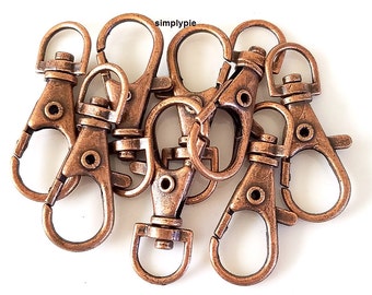 May include: A group of eight antique copper-toned metal keychains with swivel clips. The keychains are arranged in a pile, with some overlapping.