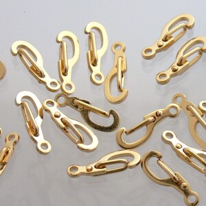May include: A group of gold-toned metal clasps or swivel hooks. The clasps are all the same design, with a rounded shape and a small loop at the top. They are commonly used for attaching jewelry, bags, or other accessories.