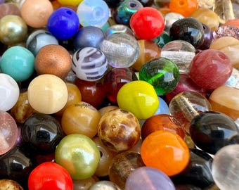 May include: A large collection of assorted round beads in various colors, textures, and finishes. The mix includes solid, translucent, pearlescent, and patterned glass or plastic spheres in shades of red, blue, yellow, green, orange, and black.