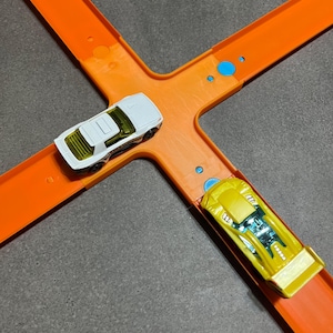 May include: Two toy cars on an orange plastic track set. A white car is on the left side of the track and a yellow car is on the right side of the track.
