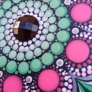 Pu&ograve; includere: Primo piano di un mandala bianco e nero con punti rosa, verdi e bianchi. Una pietra preziosa nera si trova al centro del mandala.