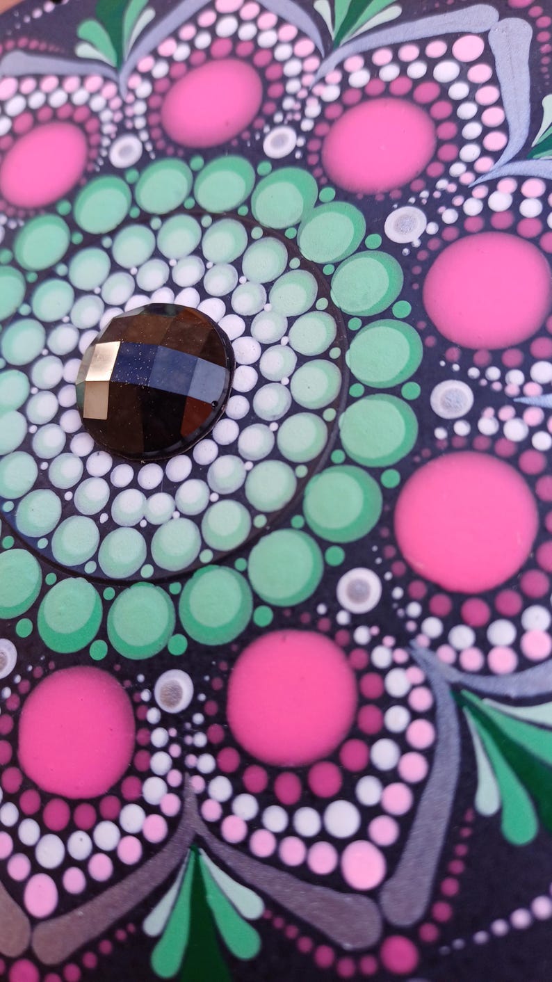 Pu&ograve; includere: Primo piano di un mandala bianco e nero con punti rosa, verdi e bianchi. Una pietra preziosa nera si trova al centro del mandala.
