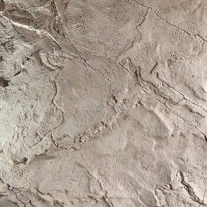 Op de afbeelding: Een close-up van een lichtgrijs, getextureerd oppervlak met een patroon van scheuren en lijnen. Het oppervlak heeft een ruwe, ongelijke textuur.