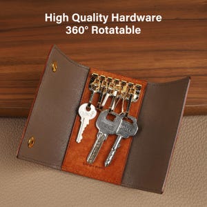 May include: A brown leather key holder with gold hardware, holding several keys. The key holder is open, revealing the keys and the interior design. The text "High Quality Hardware 360&deg; Rotatable" is visible at the top.