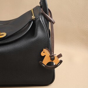 May include: Black leather handbag with a brown leather strap and a brown leather rocking horse charm.