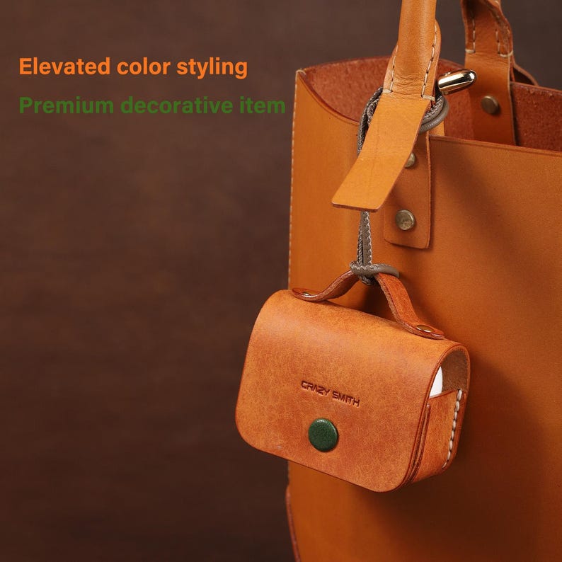 May include: A tan leather case for wireless earbuds featuring a small handle, a green circular snap button closure, and the embossed text "CRAZY SMITH". The case is attached to a tan leather tote bag with a strap and metal hardware.