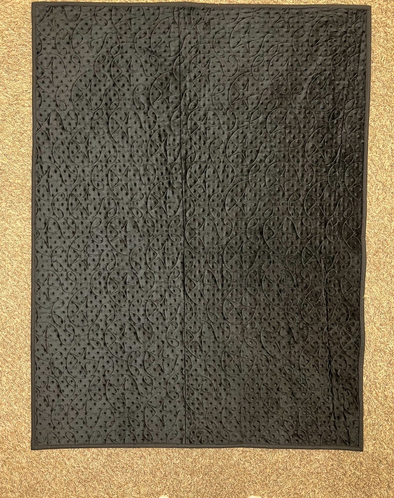 K&ouml;nnte beinhalten: Schwarzer gesteppter Stoff mit einem dekorativen Muster aus Wirbeln und Punkten.