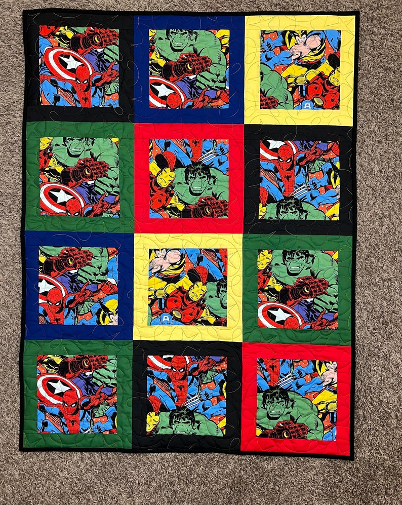 K&ouml;nnte beinhalten: Eine bunte Quiltdecke mit Patchwork-Muster, die verschiedene Marvel-Superhelden zeigt, darunter Spider-Man, Hulk, Captain America und Iron Man.