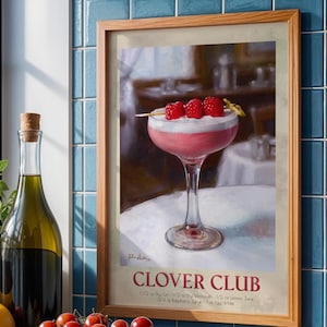 May include: A framed print of a Clover Club cocktail. The pink drink is topped with white foam and three raspberries on a toothpick. The print has a wooden frame and includes the cocktail's ingredients.