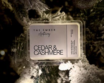 Puede incluir: Una vela blanca en un recipiente transparente con una etiqueta que dice "THE EMBER Apothecary CEDAR & CASHMERE". La etiqueta también incluye el texto "Vanilla sugar blends with jasmine, and orchid selling into a cozy base of cedarwood, vanilla, and musk. 100% Natural Soy Wax Made in USA."