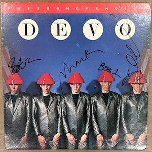 May include: A vinyl record cover for Devo's Freedom of Choice featuring five individuals in metallic silver jackets and red tiered hats against a blue background with American flags. The cover includes the text DEVO and several black ink signatures.