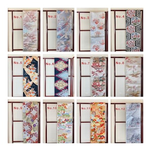 Puede incluir: Una colección de doce cinturones obi japoneses, cada uno exhibido en un marco de madera. Los cinturones presentan varios patrones, incluyendo diseños florales, geométricos y de paisajes. Los colores varían de suaves pasteles a tonos vibrantes, mostrando el arte textil japonés tradicional.