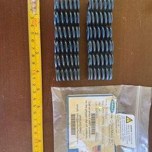 Può includere: Due pile di molle elicoidali blu accanto a un metro a nastro. Le molle sono alte circa 7.6 cm. Un sacchetto di plastica trasparente contiene un'etichetta del prodotto con il testo "DANLY SPRING 750 X 1.25-BLUE".