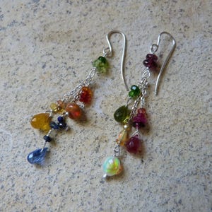 May include: A pair of dangle earrings featuring silver-toned ear wires and delicate silver chains. Each earring is adorned with a cluster of multi-colored, faceted gemstone beads in shades of blue, yellow, orange, green, red, and white.