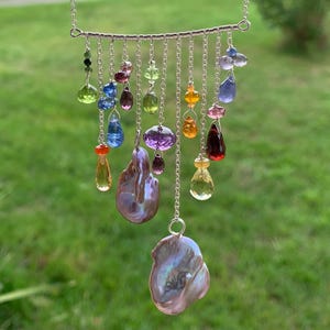 May include: A silver necklace featuring a variety of colorful gemstones and two large, iridescent baroque pearls. The gemstones include a range of colors, from green and blue to purple and orange, suspended from delicate chains.