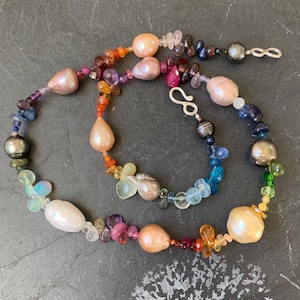 May include: A colorful necklace featuring a variety of gemstones and pearls. The necklace includes large, irregularly shaped pearls in shades of pink and white, interspersed with smaller, colorful beads. The clasp is silver.