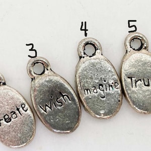 May include: Six silver-toned oval charms with the words "Unite", "Create", "Wish", "Imagine", "Trust", and "Live" engraved on them. Each charm has a small loop at the top for attaching to a necklace or bracelet. The charms are ideal for jewelry making.