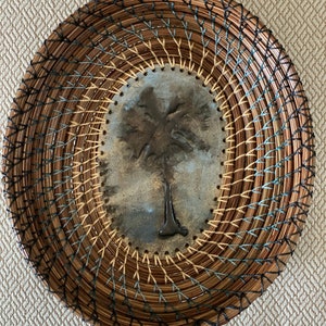 May include: A woven oval basket with a brown, tan, and blue design. The center of the basket features a metal palm tree design.