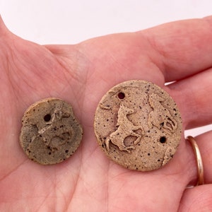 May include: Two ceramic round ornaments with a brown speckled glaze. Each ornament features a raised design of a horse. One ornament has a single horse, the other has two horses.