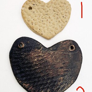 May include: Two heart-shaped ornaments. The top one is tan with a textured surface and a small hole. The bottom one is dark brown with a textured surface and two holes. These could be used as pendants or decorative accents.