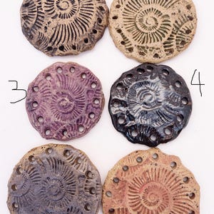 May include: Six handmade ceramic pieces with a spiral design and small holes around the edges. The pieces are in various colors, including brown, tan, purple, black, and peach. The spiral design is raised, creating a textured surface.