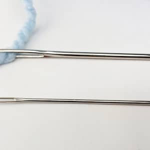 May include: Two silver sewing needles, one threaded with light blue yarn. The needles are different sizes.
