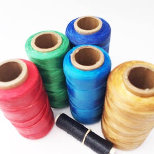 May include: Five spools of thread in red, green, blue, and gold colors. The spools are arranged in a semi-circle with a black thread spool in the center.