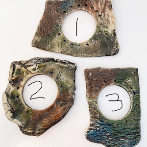 May include: Three irregular ceramic pieces with textured, mottled surfaces in shades of green, brown, and blue. Each piece features a large central circular cutout surrounded by a ring of small, evenly spaced holes, labeled with the numbers 1, 2, and 3.