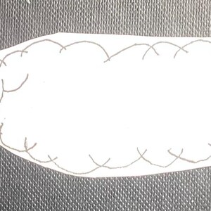 K&ouml;nnte beinhalten: Ein wei&szlig;er Filzwurm mit einer roten Nase und einem schwarzen Umriss. Der Wurm liegt auf einer grauen Oberfl&auml;che.