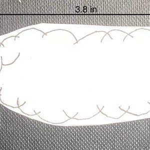K&ouml;nnte beinhalten: Wei&szlig;er Filz-Applique einer Raupe mit roter Nase und schwarzen Augen. Die Raupe ist 9,7 cm lang.