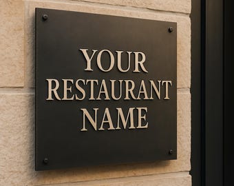 Könnte beinhalten: Ein schwarzes rechteckiges Schild mit den Worten "YOUR RESTAURANT NAME" in einer Serifenschrift. Das Schild ist mit vier Schrauben an einer hellen Steinmauer befestigt.