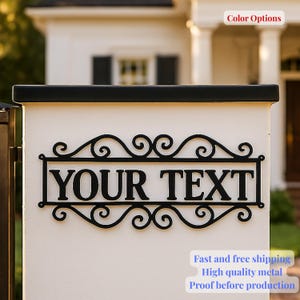 Peut inclure: Panneau en métal noir avec le texte "YOUR TEXT" dans un cadre rectangulaire avec des volutes décoratives. Le panneau est monté sur un pilier blanc avec un dessus noir. L'arrière-plan montre une maison.