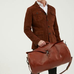 May include: A brown leather duffel bag with a long strap. The bag has a flap closure with a buckle and a metal hook.