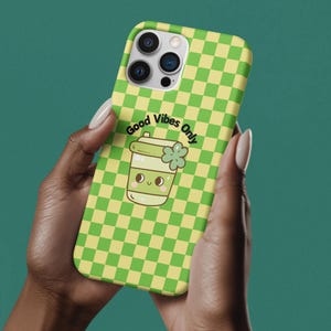 May include: A green and yellow checkered phone case with a cartoon green cup with a clover on top and the text "Good Vibes Only".