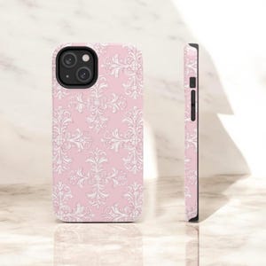 May include: A pink phone case with a white damask pattern. The case has a cutout for the camera lens.