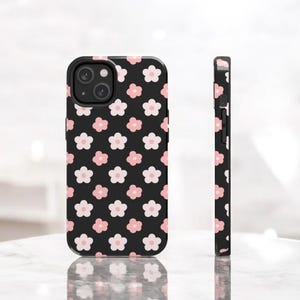 May include: A black phone case with a pink and white floral pattern. The case has a camera cutout and a raised lip around the edges.