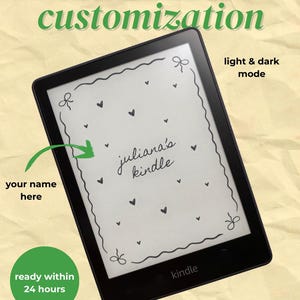 Könnte beinhalten: Ein schwarzer Kindle E-Reader mit einem angepassten Sperrbildschirm. Der Bildschirm zeigt einen weißen Hintergrund mit schwarzen Herzen und dekorativen Elementen. Auf dem Bildschirm steht "juliana's kindle". Das Bild enthält auch den Text "kindle & kobo lockscreen customization."