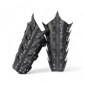 Puede incluir: Un par de protectores de brazo de cuero negro con un diseño de escamas de dragón. Los protectores están tachonados con remaches plateados y tienen un diseño puntiagudo y espinoso.
