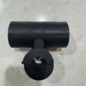 May include: A black, cylindrical object with a circular opening and a connecting piece. The object appears to be made of a solid material and is designed to hold or connect to another object. The design is simple and functional.