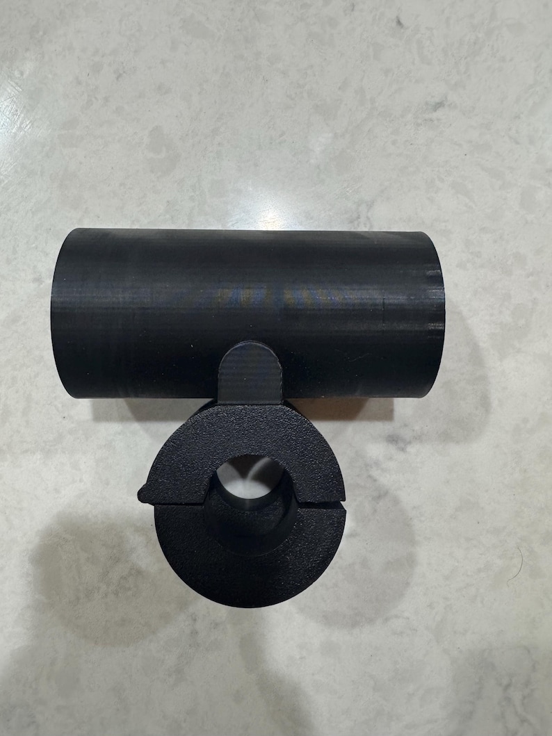 May include: A black, cylindrical object with a circular opening and a connecting piece. The object appears to be made of a solid material and is designed to hold or connect to another object. The design is simple and functional.