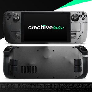 May include: A handheld gaming console with a black screen displaying the text "creatiivelabs" in white and green. The console has a gray and black design with buttons and controls on both sides. The bottom of the console is also visible.