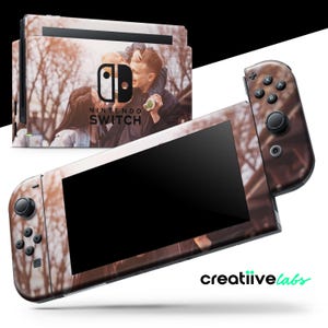 May include: A Nintendo Switch console skin with a photo of two people in a forest. The skin features a brown and green color scheme with a blurry background. The text "Nintendo Switch" is visible on the skin.