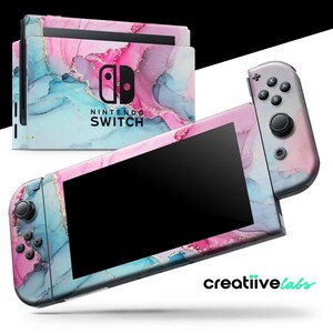 May include: Nintendo Switch console and controllers with a custom skin featuring a pink, blue, and gold marble design. The console has the Nintendo Switch logo and the text "SWITCH". The controllers have black buttons and joysticks.