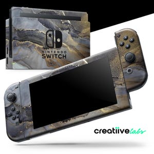 Pode incluir: Uma consola Nintendo Switch e a sua base com uma capa personalizada com um design marmoreado em tons de cinza, preto e dourado. A consola tem botões pretos e um ecrã preto. O texto "NINTENDO SWITCH" é visível.