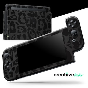 Puede incluir: Consola y mando de Nintendo Switch negros y grises con un diseño de estampado de leopardo. La consola tiene una pantalla y botones, y el mando tiene botones y una palanca de mando.