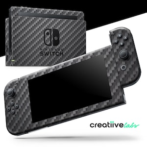 Puede incluir: Una consola Nintendo Switch y sus mandos con un diseño de fibra de carbono. La consola y los mandos están cubiertos con un patrón tejido gris y negro. El logotipo de Nintendo Switch es visible en la consola. La marca "creatiive labs" está en la esquina inferior derecha.