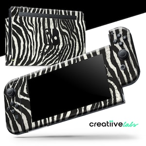 Könnte beinhalten: Eine Nintendo Switch-Konsole und Controller mit einem schwarz-weißen Zebra-Print-Design. Konsole und Controller werden vor einem weißen Hintergrund gezeigt. Der Text "SWITCH" ist auf der Konsole zu sehen.